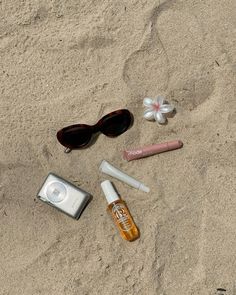 an assortment of personal items laid out in the sand with sunglasses and eyeglasses