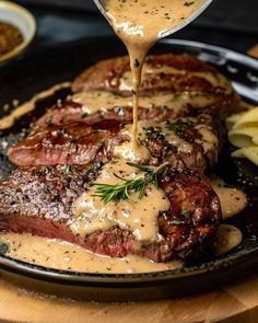 steak with gravy being drizzled over it on a black plate