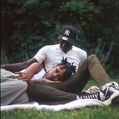 a man and woman laying on top of each other in the grass with trees behind them