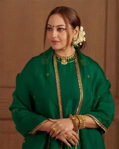 a woman in a green outfit with gold jewelry on her neck and hands behind her back