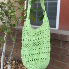 a green crocheted bag hanging from a tree in front of a brick building