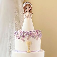 a white wedding cake with purple flowers and a figurine on the top tier