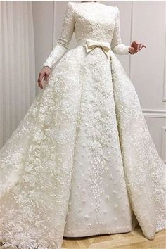 a woman in a white wedding dress with long sleeves and a bow at the waist