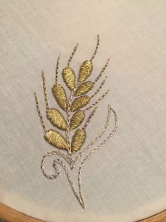 a close up of a embroidery on a piece of cloth with gold thread and leaves