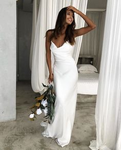 a woman in a white dress standing next to a bed