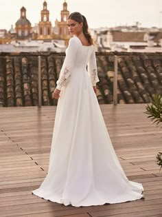 a woman in a white wedding dress standing on a wooden deck looking off into the distance