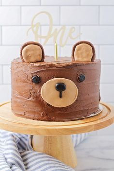 a cake with chocolate frosting and teddy bears on top, sitting on a wooden stand