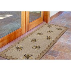 a door mat with two bees on it in front of a glass door and tile floor