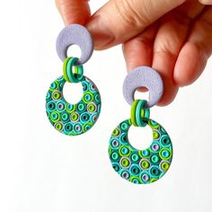 a pair of earrings is being held in the air by someone's hand and they are made out of polymer