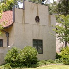 an old building with a round window in the corner and bushes around it on a sunny day