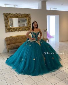 a woman in a blue ball gown standing next to a couch and mirror with her hands on her hips