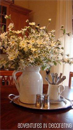 a white pitcher filled with flowers on top of a wooden table