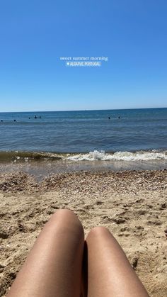 someone is sitting on the beach with their feet in the sand looking out at the ocean