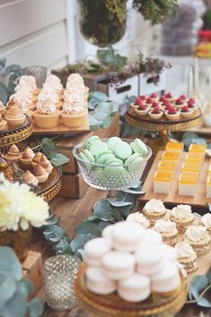 an assortment of desserts and pastries displayed on wooden trays with greenery