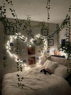 an unmade bed with lights and plants hanging from the headboard, along with pictures on the wall