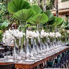 a long table topped with lots of tall vases filled with white flowers