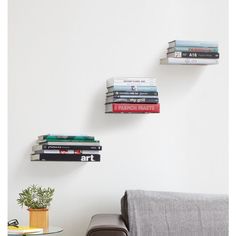 three books are stacked on top of each other in front of a white wall and a couch