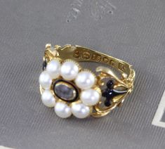 "An immaculate antique Georgian mourning ring, crafted in 18k yellow gold with a lustrous split pearl halo around the center compartment which holds a momento of woven hair under crystal. The shoulders are delicately articulated in a baroque scroll design, accented by glossy black enamel, and the ring is fully hallmarked for 18k, London manufacture, and letter dated 1828. Measuring approximately 1/2\" north to south at the center front, tapering through the shoulders to 2.22 mm at the center bac Georgian Wedding Ring, Etruscan Jewelry, Georgian Ring, Enchanted Jewelry, Vintage Jewlery, Black Pearl, Gold Pearl, Jewelry Inspo, Black Enamel