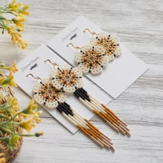 two pairs of beaded earrings sitting on top of a wooden table next to flowers