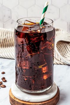 a glass filled with liquid sitting on top of a wooden coaster next to coffee beans