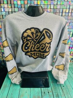 This comfortable cheer mom sweatshirt is perfect for those chilly practice sessions. Made with soft fabric and a relaxed fit, it provides both warmth and style. Stay warm and show your support in this must-have sweatshirt for any proud cheer mom. Casual Tops For Cheerleading In Fall, Fall Team Spirit Sweatshirt With Screen Print, Fall Sports Fan Sweatshirt With Graphic Print, Fall Sports Fan Graphic Sweatshirt, School Spirit Fleece Sweatshirt For Sports Season, Cheerleading Fan Apparel Tops For Fall, Varsity Sweatshirt For Cheerleading In Fall, Fall Cheerleading Top With Letter Print, Fleece Sweatshirt For School Spirit