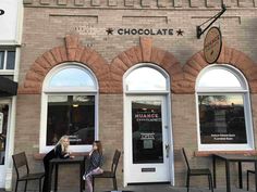 two women sitting at tables in front of a chocolate shop