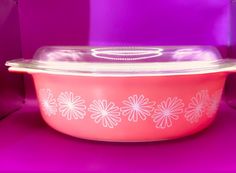 a pink casserole dish with white flowers on the side and purple back ground