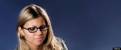 a woman wearing glasses looking at her cell phone while sitting in front of a blue background