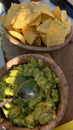 two bowls filled with guacamole and tortilla chips on a table