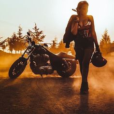 a woman walking down a dirt road next to a motorcycle