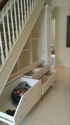 an open drawer under the stairs in a room with tile flooring and white walls