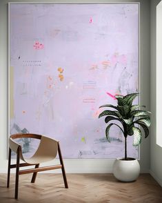 a chair and potted plant in front of a large pink painting on the wall