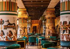 the interior of a restaurant with painted columns and green velvet chairs, along with other colorfully decorated tables