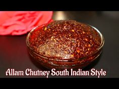 a bowl filled with chili sauce next to a red flower on a black counter top