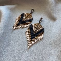 two pairs of beaded earrings on top of a white cloth covered surface with black and gold accents