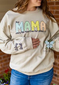 Show off your love and style with our This Mama Wears Her Heart On Her Sleeve personalized crewneck sweatshirt! Made with high-quality fabric for all-day comfort, this sweatshirt is the perfect way to express your love for your little ones. Get ready to turn heads and melt hearts with this unique and meaningful piece. Casual Crew Neck Sweatshirt For Mother's Day, Casual Long Sleeve Sweatshirt For Mother's Day, Trendy Cotton Sweater With Heart Graphic, Mother's Day Casual Long Sleeve Sweatshirt, Trendy Cotton Sweatshirt For Mother's Day, Heart On Sleeve Sweatshirt, Cotton Sweatshirt With Heart Graphic And Long Sleeves, White Cotton Sweatshirt With Heart Graphic, Long Sleeve Cotton Sweatshirt With Heart Graphic