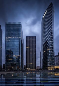 some very tall buildings in a big city at night with water reflecting off the ground