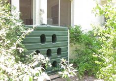 a green bird house sitting in the middle of some bushes