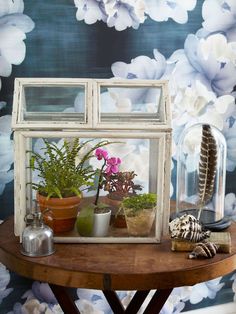 a table with flowers and plants on it in front of a wallpapered background