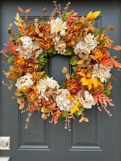 a wreath on the front door with autumn leaves and flowers hanging from it's side