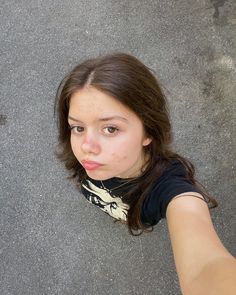 a young woman taking a selfie with her cell phone in hand and looking up at the camera