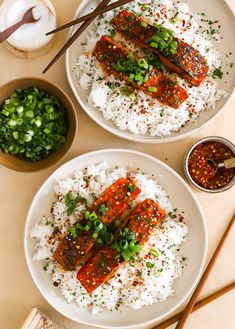 two white plates topped with rice covered in sauce and green onions next to chopsticks