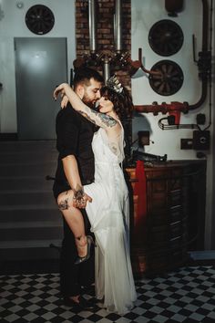 a man and woman standing next to each other in front of a wall with pipes