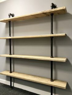 three wooden shelves with black pipe handles and two metal pipes on each shelf, against a gray wall