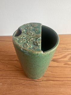 a green vase sitting on top of a wooden table with a hole in the middle