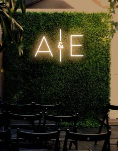 an illuminated neon sign on the side of a green wall with chairs in front of it