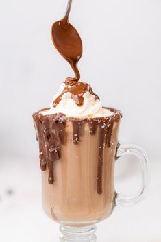 a spoon scooping chocolate into a cup with whipped cream and chocolate sauce on top