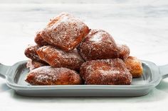 powdered sugar donuts stacked on top of each other in a gray tray with spoons