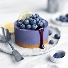 a blueberry cheesecake on a white plate with spoons and lemon wedges