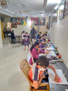 several children are sitting at a long table with artwork on the wall behind them and one child is drawing